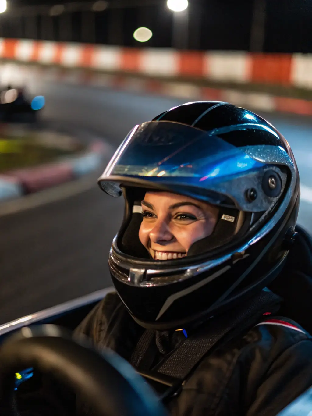A young person in a karting helmet, smiling and giving a thumbs-up, with a kart in the background on a sunny day at the ASSOCIATION TEAM RACING AURILLACOIS track.