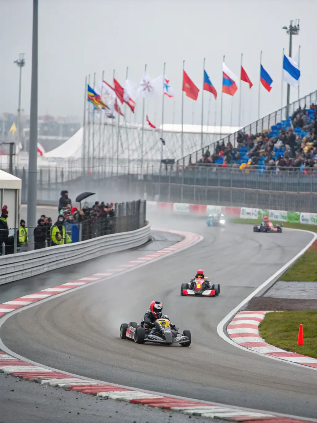 A dynamic shot of a karting race in progress, showcasing the speed and excitement of the sport, with karts closely competing on a turn and spectators cheering from the sidelines.